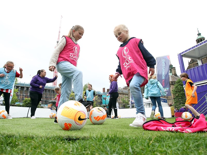 Girls playing football wearing UEFA Women's EURO 2022 bibs in the Peace Gardens in Sheffield