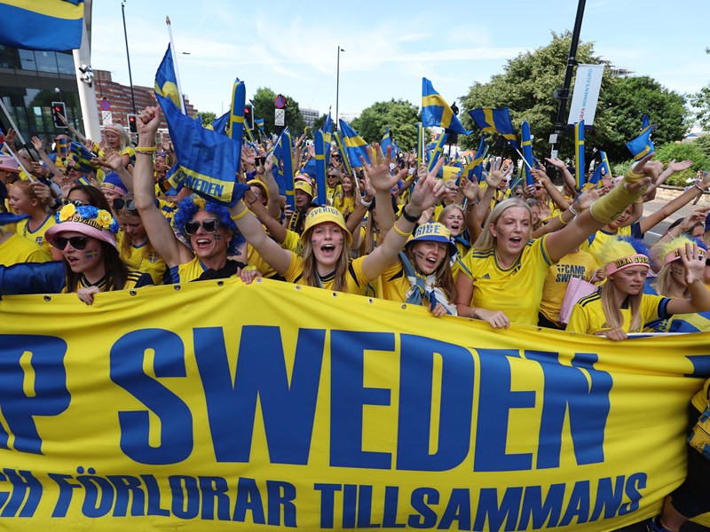 A large group of people dressed in yellow hold a large banner that say 'camp Sweden'