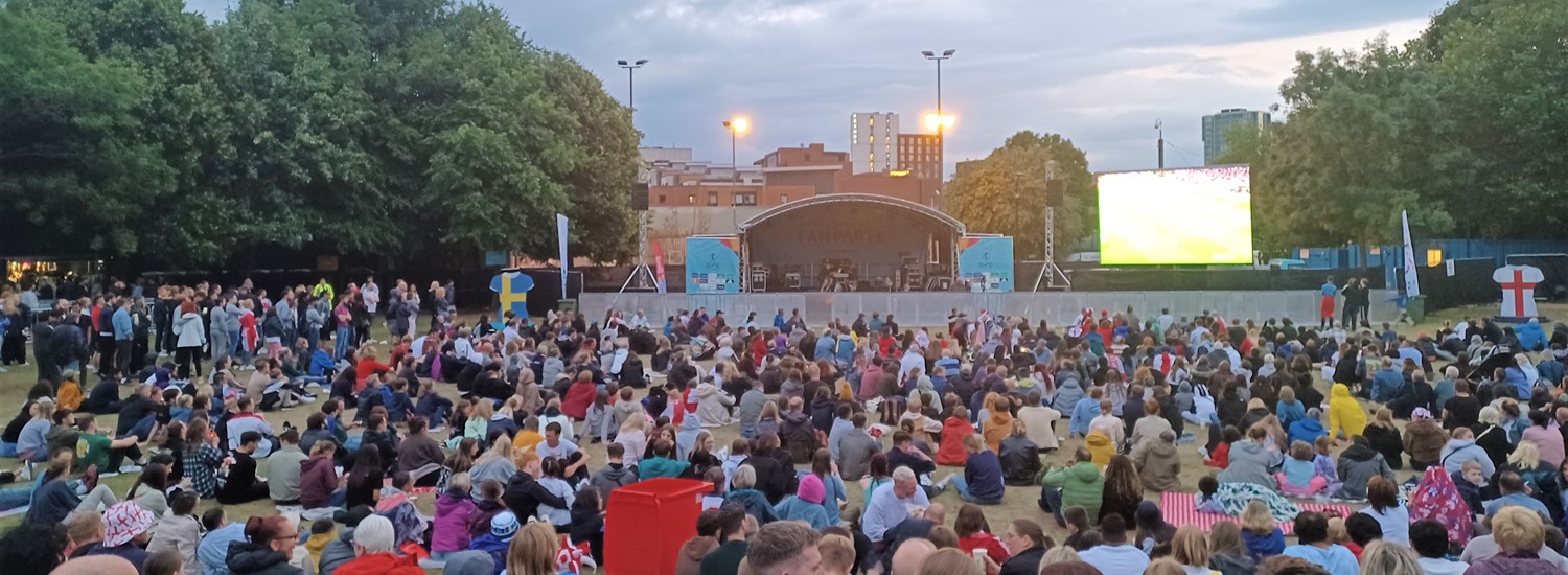 A crowd of people sitting in front of a large stage and screen on Devonshire Green in Sheffield