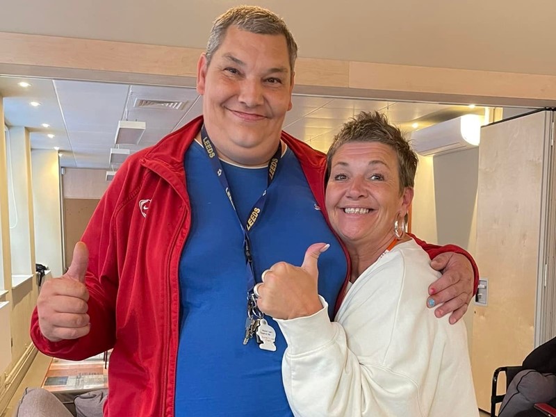 A man and woman with arm around each other hold thumbs up