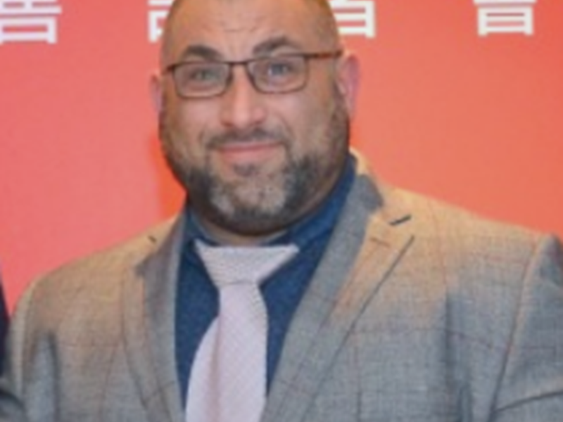 Mr Ata in suit and tie doing a thumbs up sign and slightly smiling