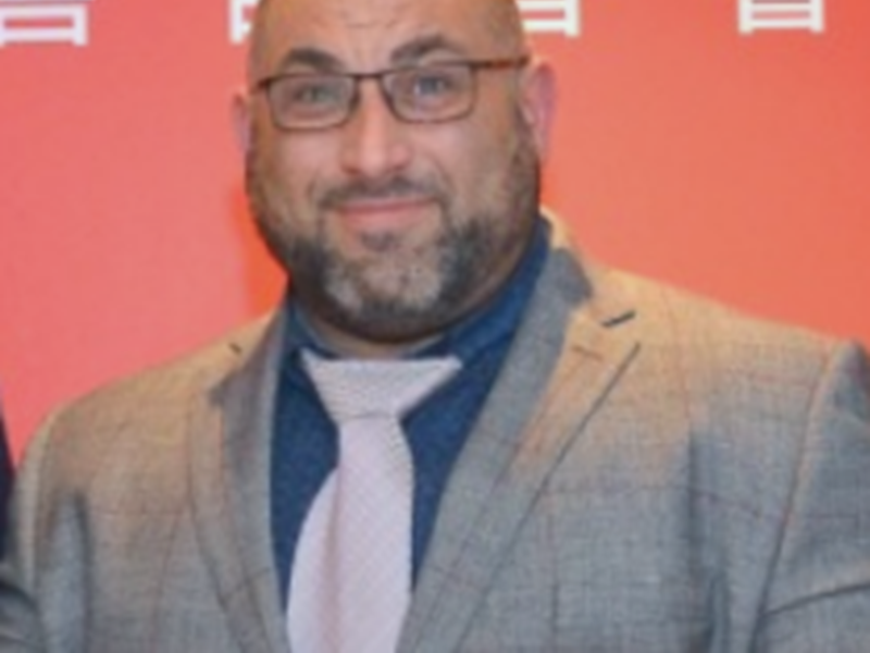 Head shot of Mr Ata in a grey suit and tie and blue shirt