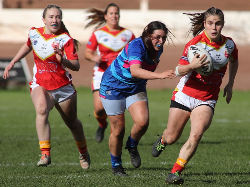 Four women playing rugby league, one is running with the ball