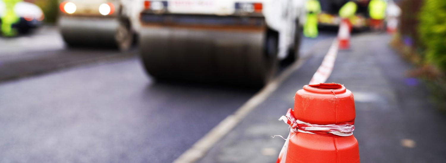 An orange cone in front of a blurred tarmac roller