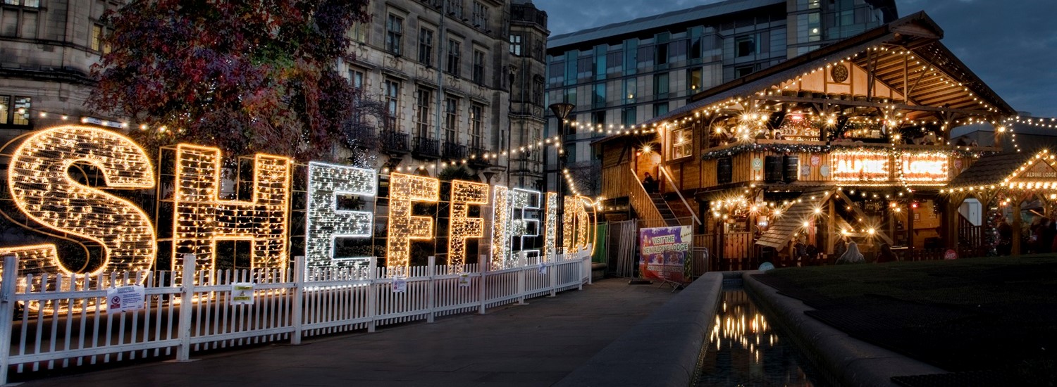 The word 'Sheffield' in gold and silver lights, a large civic building is behind it and a wooden festive bar