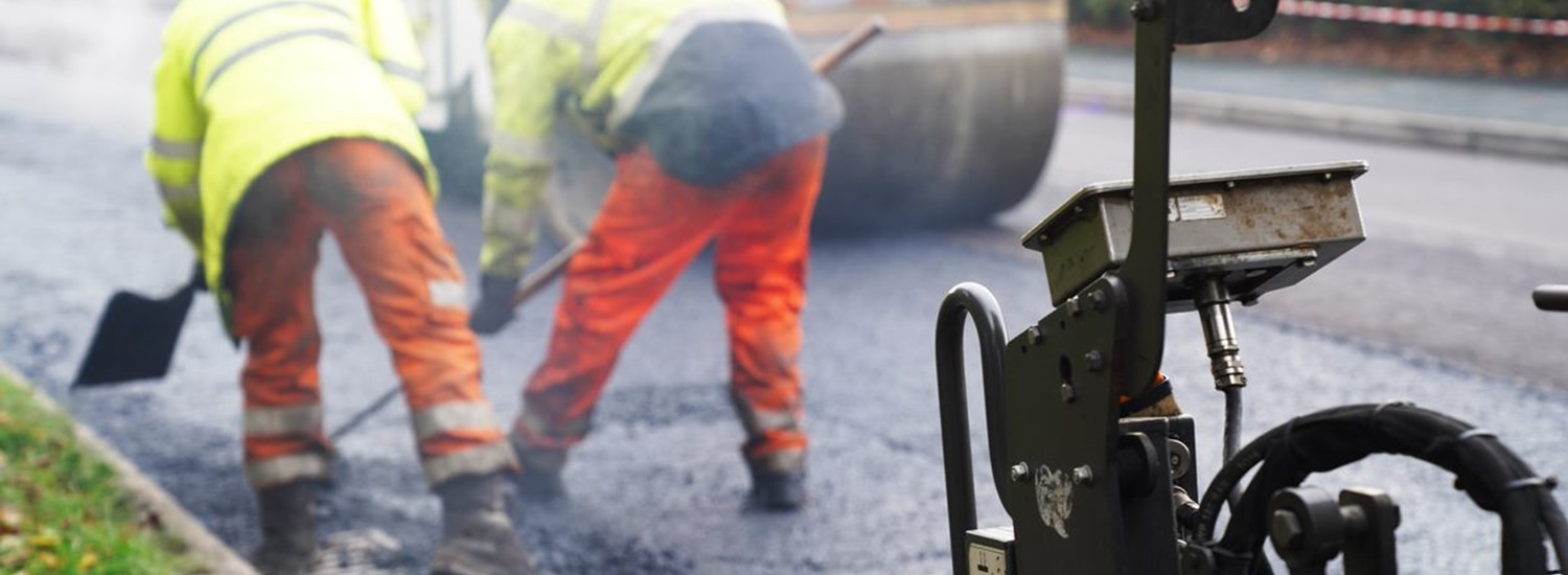 Two people in high visibility clothing lay tarmac