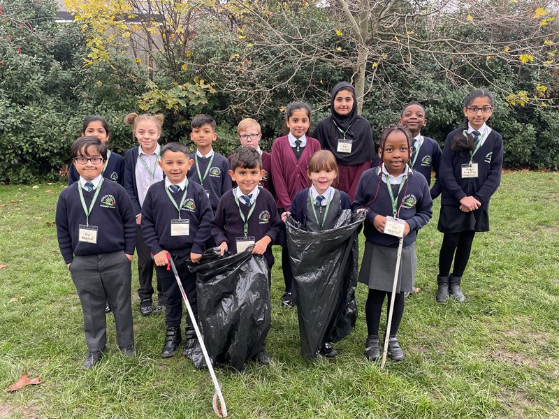 School children stand in group, some with bags and litter pickers