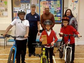 Two teachers and Cllr Mazher Iqbal with 3 pupils and their bikes in a school hall