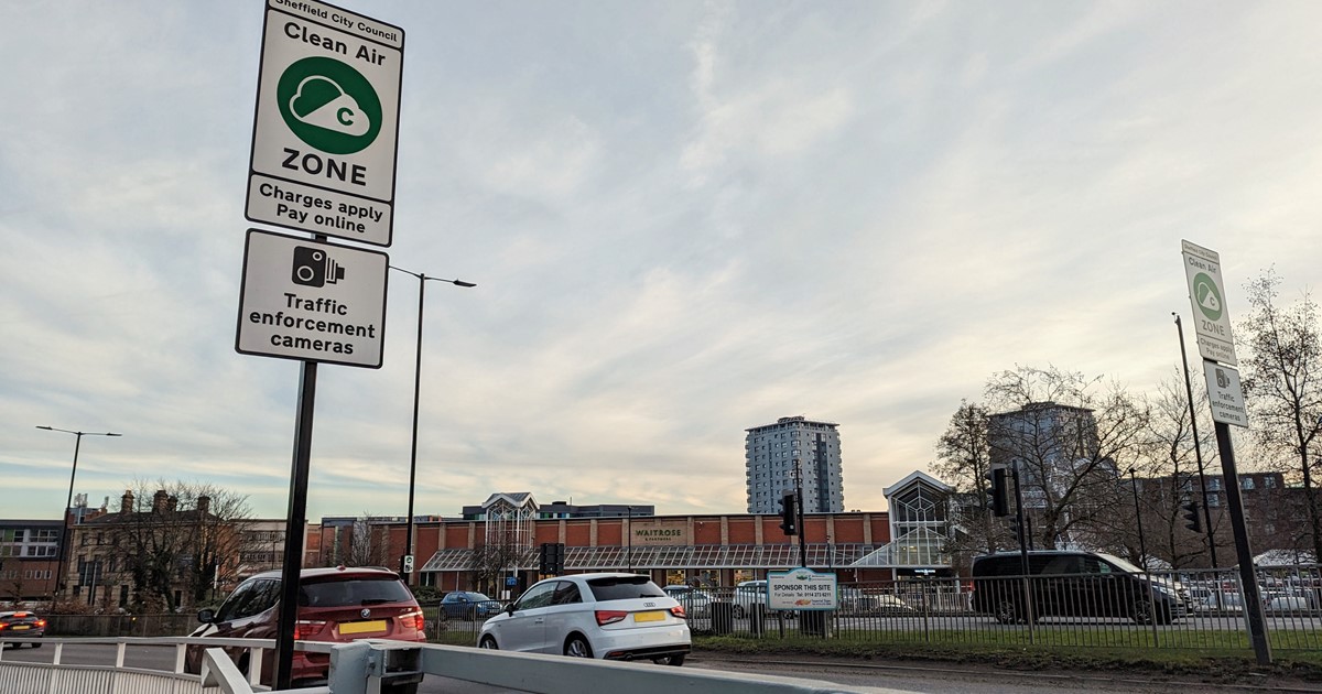 A white road sign informs drivers on the side of the road that they could be liable for a Clean Air Zone charge if their vehicle is not compliant. 