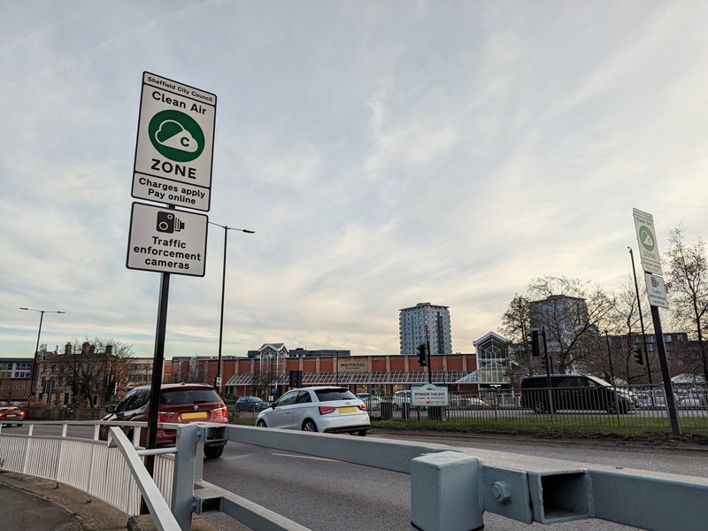 A white road sign informs drivers on the side of the road that they could be liable for a Clean Air Zone charge if their vehicle is not compliant. 
