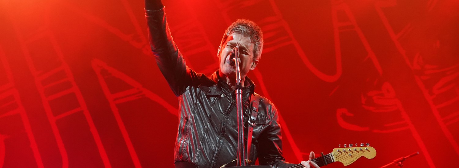 Picture of Noel Gallagher behind a microphone with a guitar