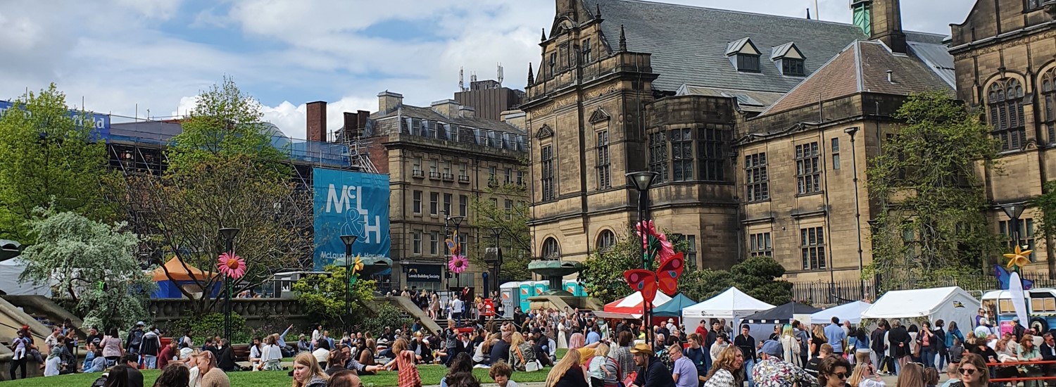 Sheffield Town Hall and Peace Gardens, showing people sat on the green grass in crowds