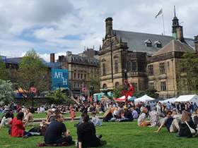 Sheffield Town Hall and Peace Gardens, showing people sat on the green grass in crowds