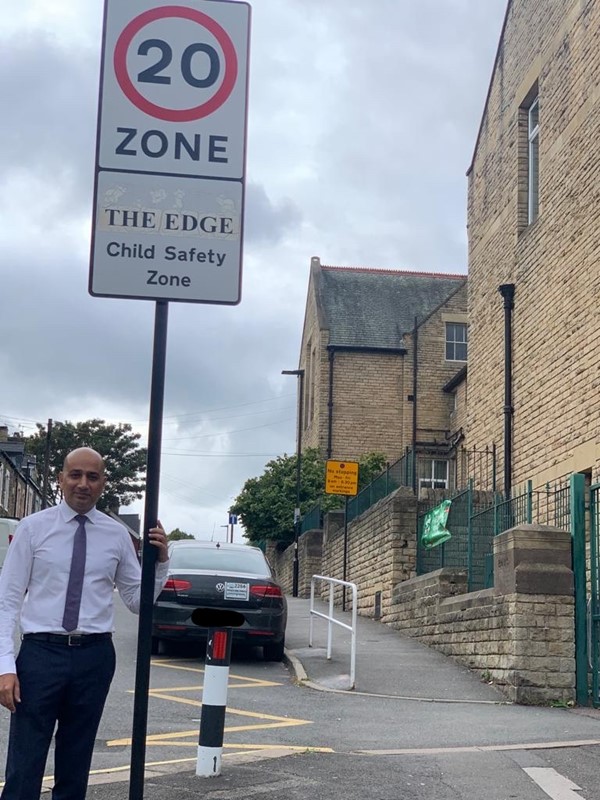 Cllr Mazher Iqbal next to a road sign that says '20 zone'