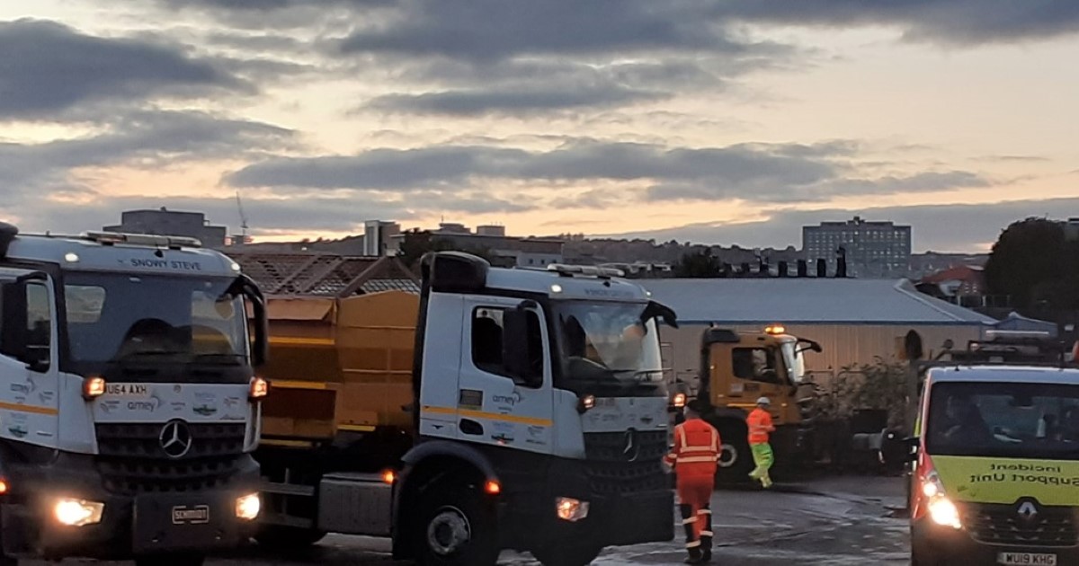 Two gritter lorries at dusk at works depot with pink and blue dusk sky