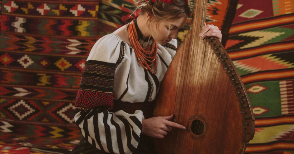 Ukrainian singer Maryna Krut is dressed in traditional dress and posing with a bandure, a stringed instrument.