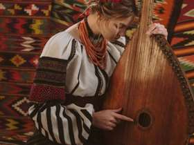 Ukrainian musician Maryna Krut is dressed in traditional dress and posing with a bandura instrument.