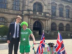 Councillor Tom Hunt and John Burkhill wearing his green wig, and pushing his pram, outside Sheffield Town Hall