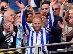 Sheffield Wednesday captain Barry Bannan raising his hands up in the stands, wearing a blue and white striped Sheffield Wednesday top
