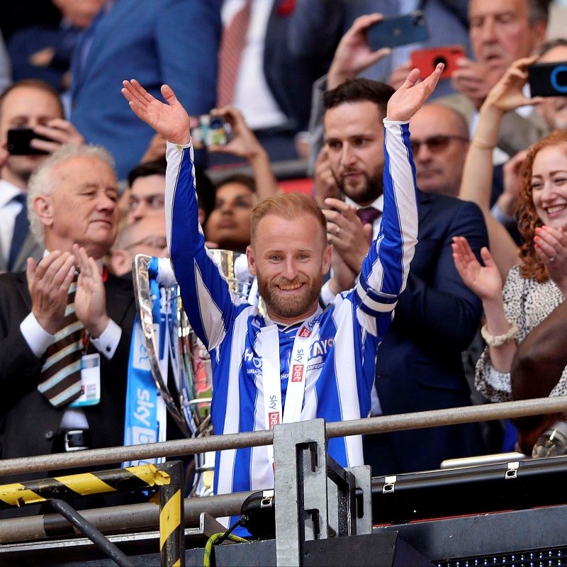 Sheffield Wednesday captain Barry Bannan raising his hands up in the stands, wearing a blue and white striped Sheffield Wednesday top