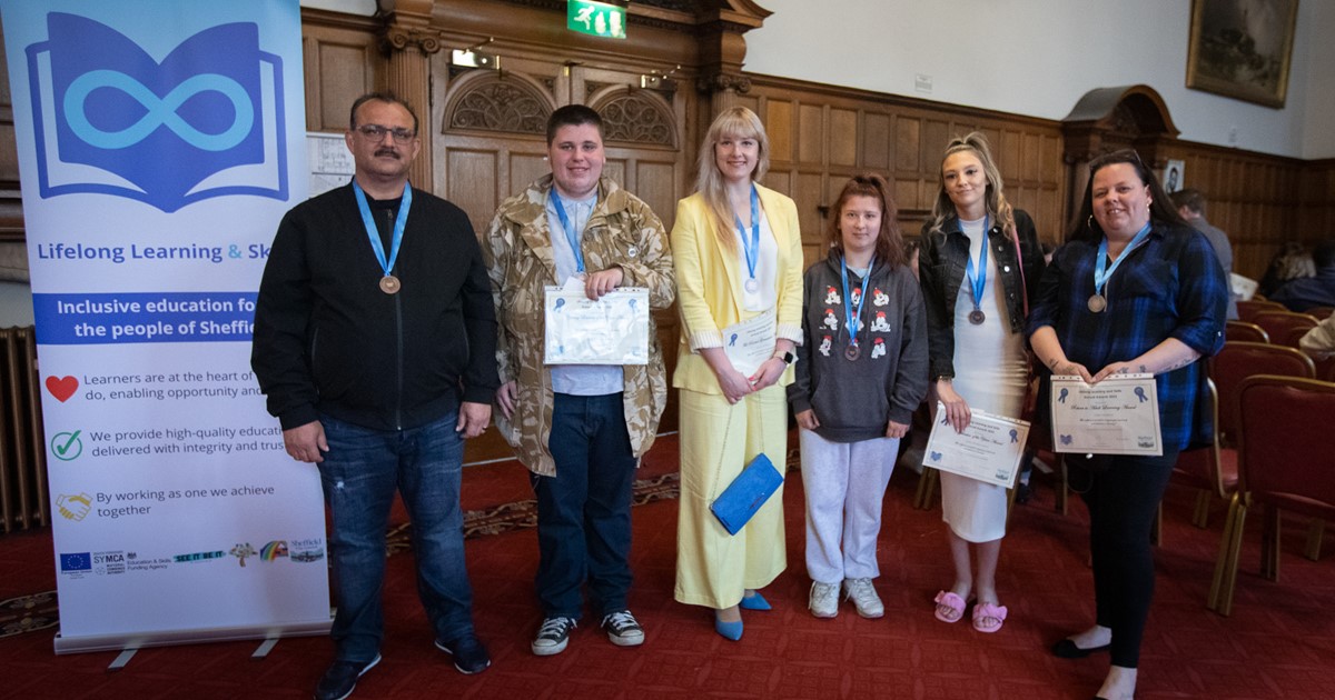 Six people stand in a line in front of a banner for Lifelong Learning in Sheffield Town Hall. 