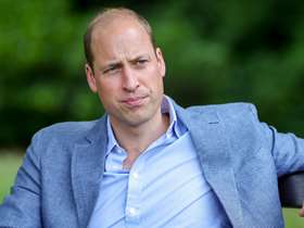 Prince William sat on a bench wearing a light blue shirt and a darker blue blazer 