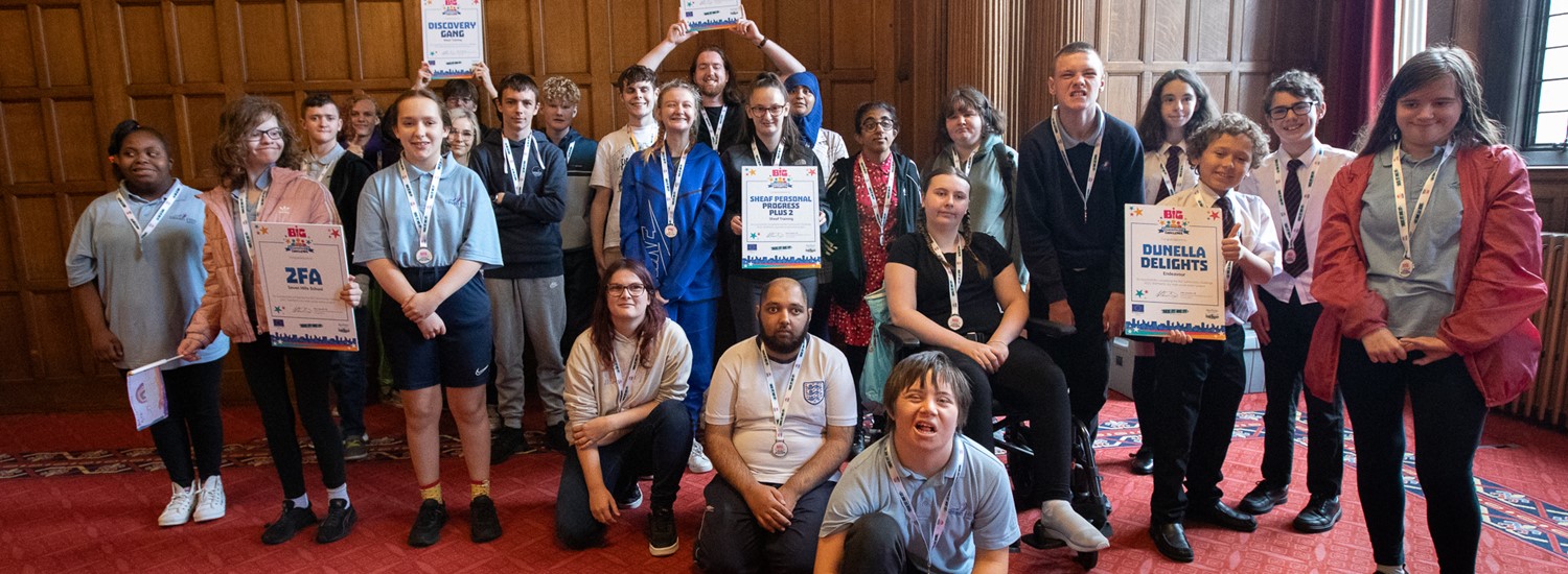 Group of students with their certificates and medal in the town hall with wooden panelling behind them and a red carpet