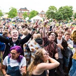 A crowd of people facing the camera with their hands in the air whilst they watch a band