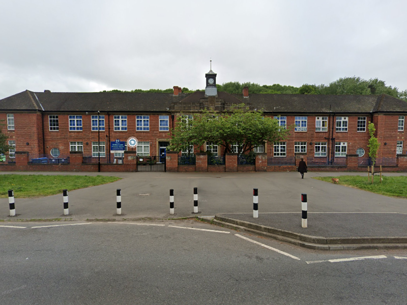 red brick school building with white- framed windows, grass and black and white road bollards in the foreground