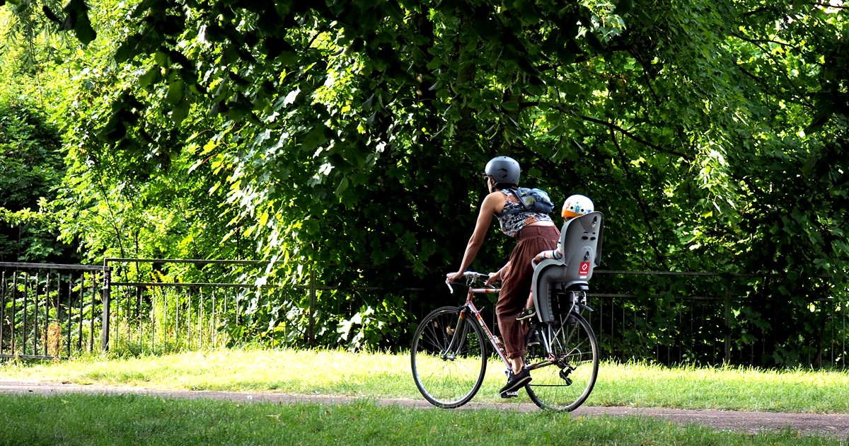 A mother and child cycle through a park