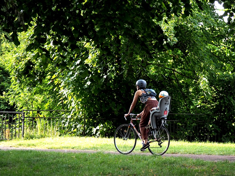 A mother and child cycle through a park