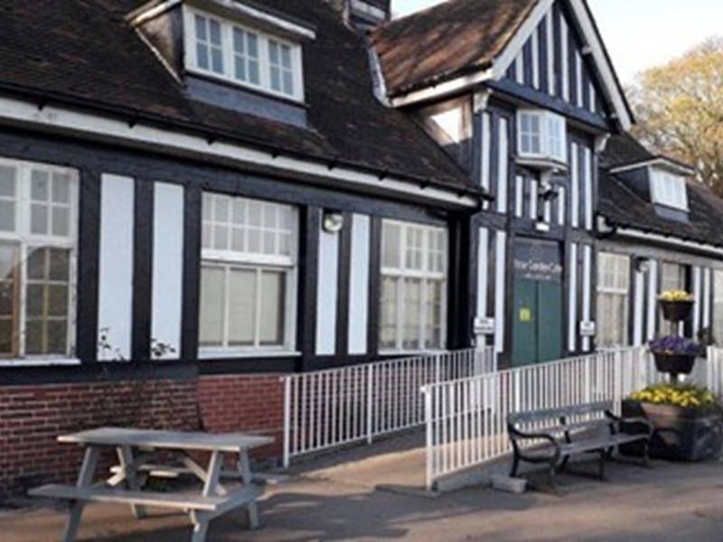 Rose Garden Café building front elevation with green door, black and white exterior and brick, white railings along outdoor path