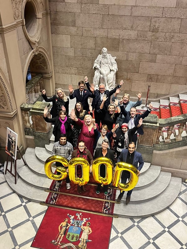 Officers and councillors stand on the bottom of the main staircase in Sheffield Town Hall with arms in the air celebrating the Ofsted result with four gold balloons held at the fron saying 'GOOD'