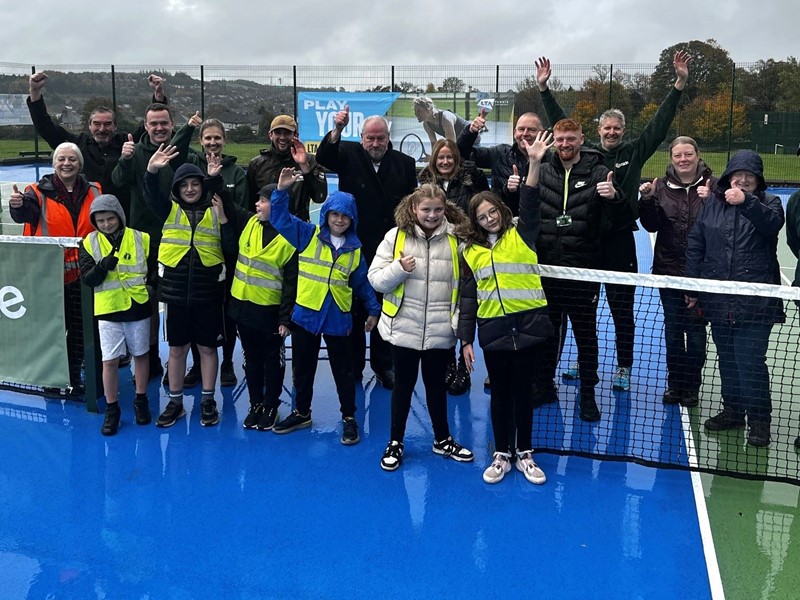 Schoolchildren in front row on tennis court in yellow hi-vis with SCC officers, Councillor Richard Williams, Friends of Hollinsend Park and LTA officers 