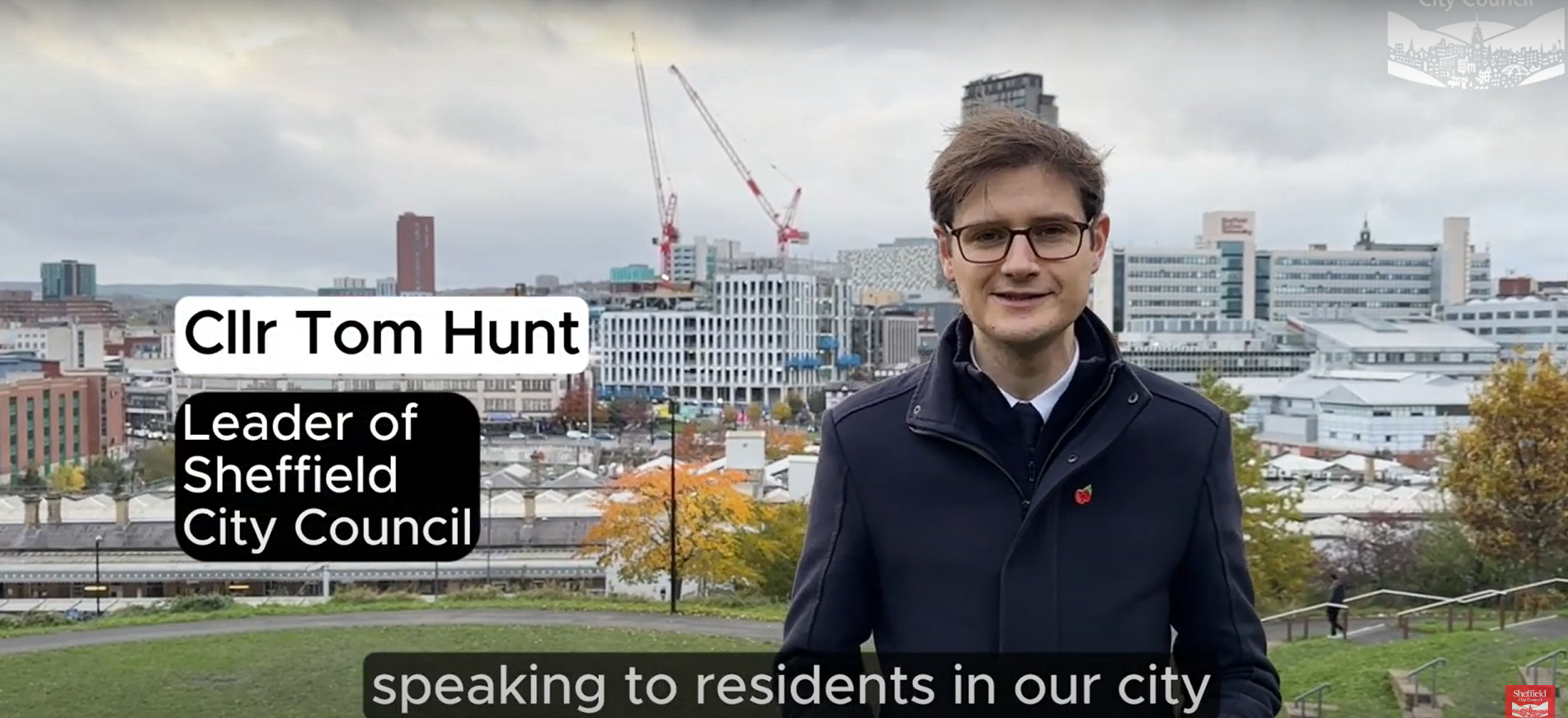 Councillor Tom Hunt, stood infront of a Sheffield skyline, showing cranes and buildings. Tom is wearing a dark coat with a red poppy badge for Remembrance Sunday.  
