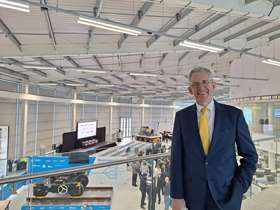 Councillor Martin Smith, stood inside the AMRC at the University of Sheffield, behind him are people enjoying the groundbreaking event which shows  a robot resembling a vehicle