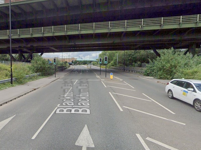 The top deck of the Tinsley Viaduct runs over the top of a two lane road in the foreground with a traffic light showing a red and amber light