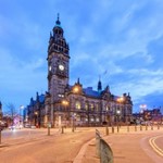 Sheffield Town Hall lit up at dusk with road and square in foreground against a blue sky