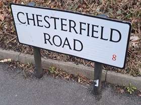 A street sign for Chesterfield Road set in concrete with brown foliage behind it
