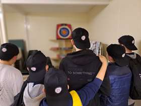 Youngsters wearing baseball caps facing a dartboard with their backs to the camera