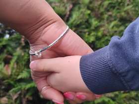 A mother and child hold hands in front of green foliage