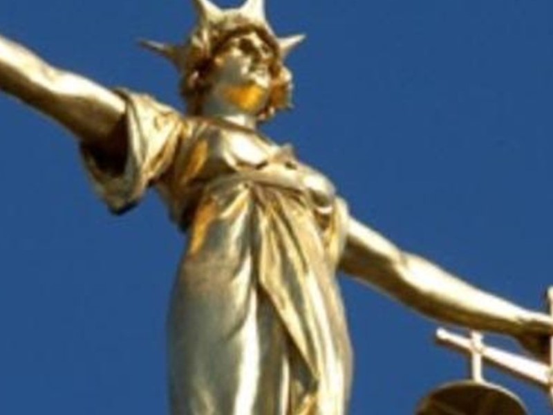 A statue of the Scales of Justice in front of a clear blue sky
