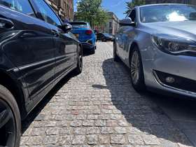Cobbled street with a car double parked next to another car