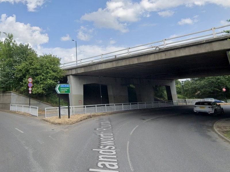 Picture of a road with a car going underneath a bridge