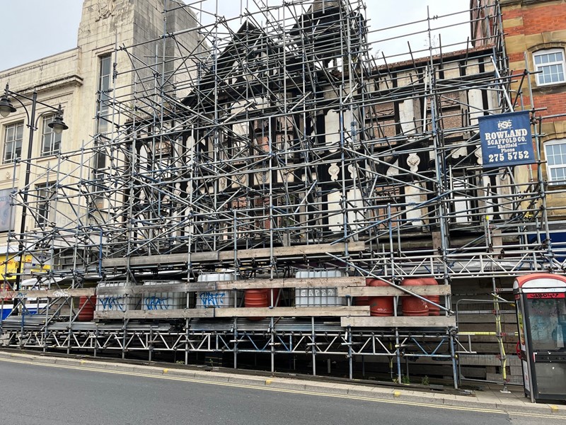 The black and white mock-tudor facade of the building on Haymarket covered in scaffolding with buildings on either side