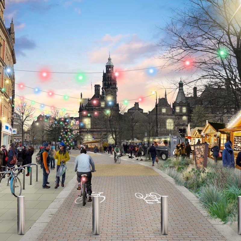 An artist impression showing Pinstone Street in Sheffield with the Town Hall in the background and the Christmas Market on the right hand side. The street has pedestrians and cyclists on it with hanging lights above the street.