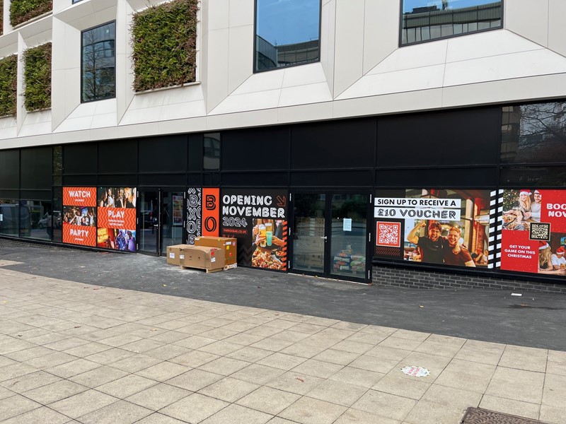 The front of the unit in the Gaumont building showing the black frontage with colourful posters, above are windows with white surrounds and plants in between.