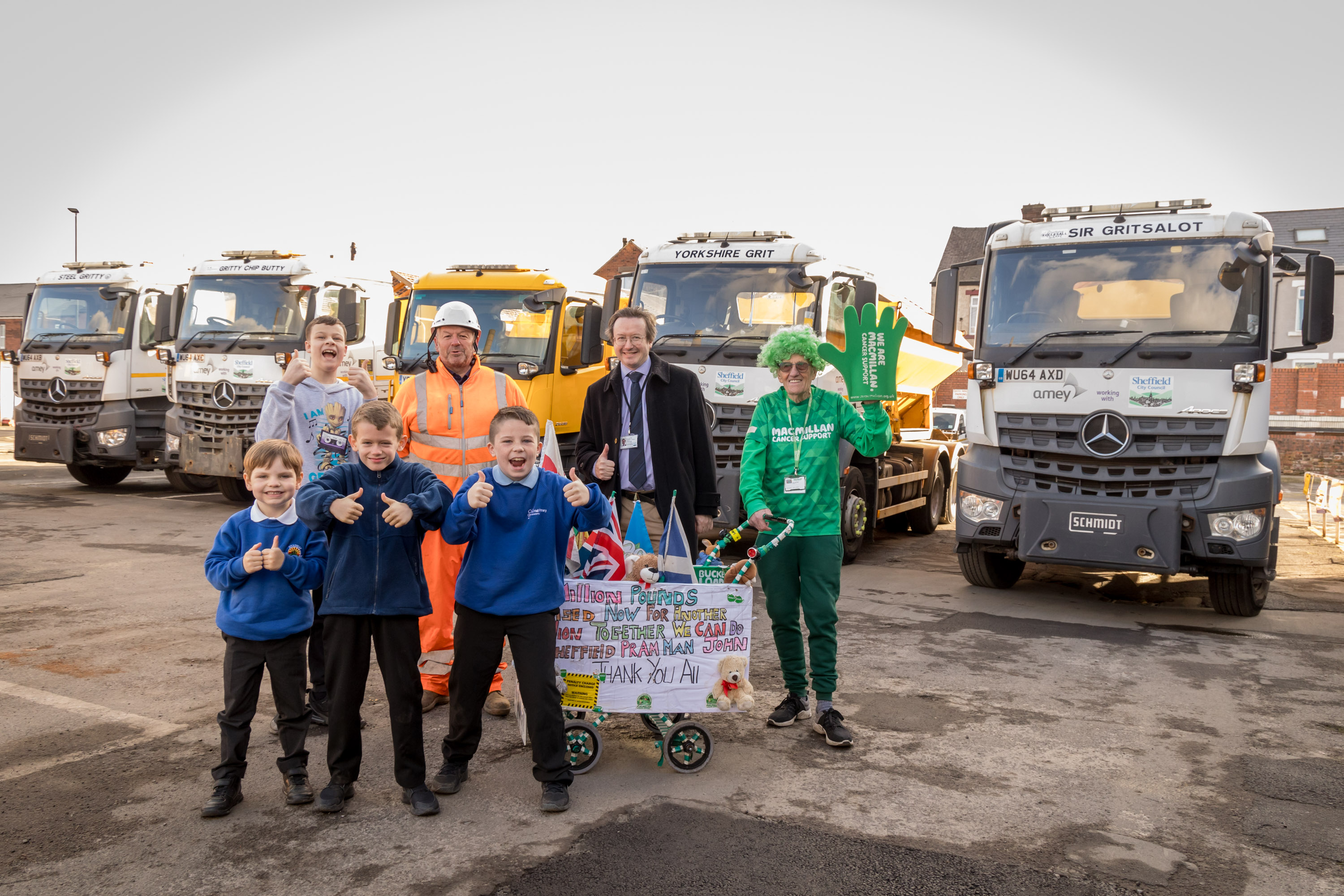 A picture of children and adults stood in front of a line of white and orange gritters