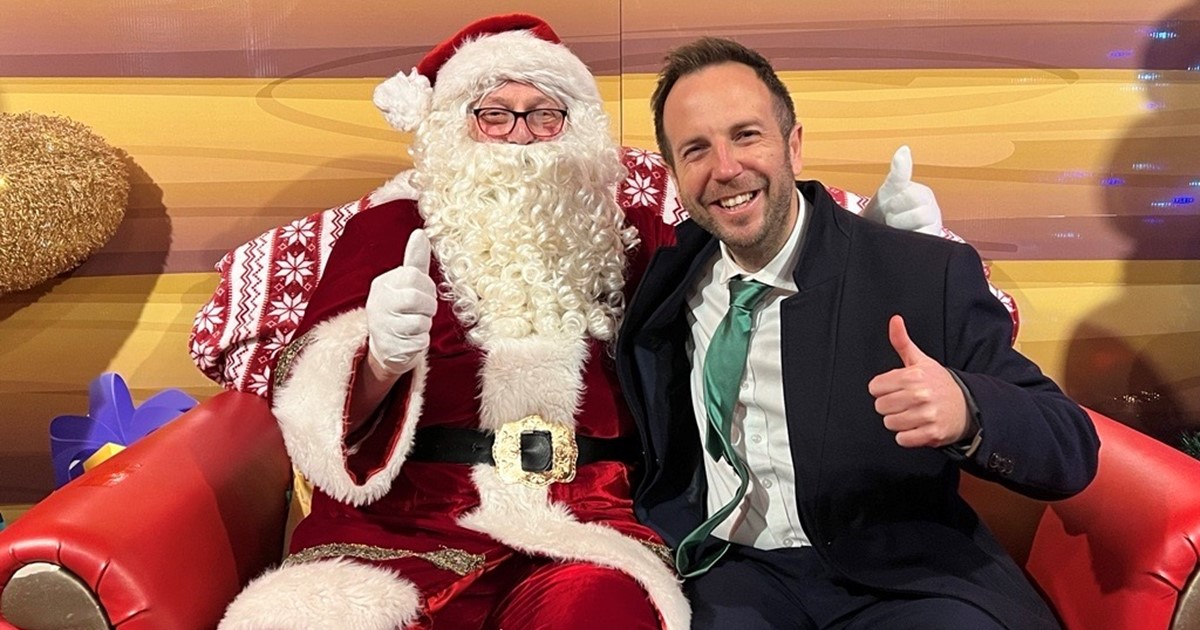 Cllr Ben Miskell and Father Christmas site in Santa's grotto, both are looking at the camera giving a thumbs up