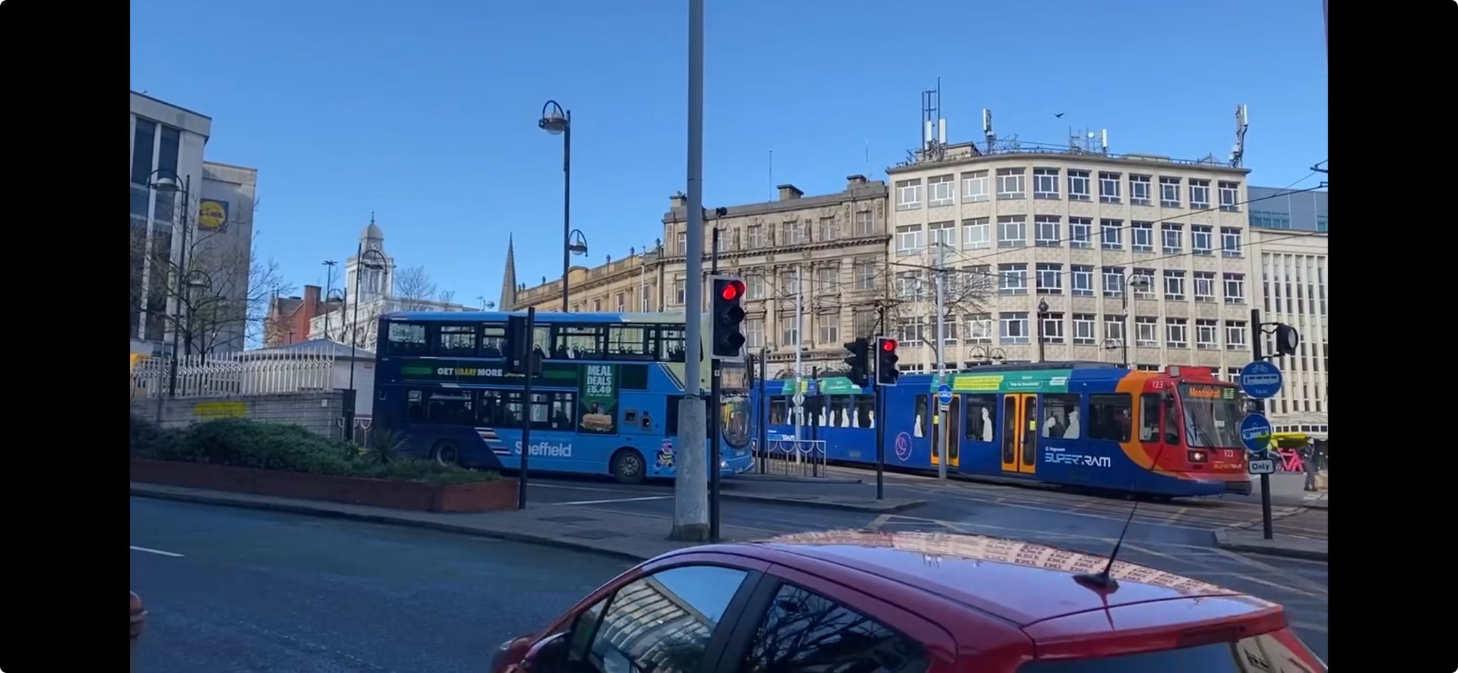 A view of Sheffield city centre with a car in the foreground, bus in the middle ground along with a Supertram, in the background are some office type buildings